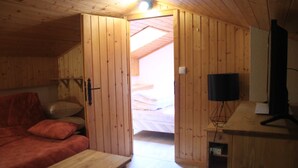 A wooden room with a bed, a red sofa, a TV, and a wooden desk.