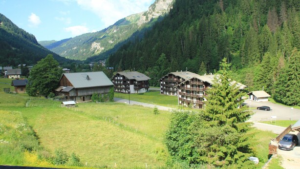 A mountain village with traditional wooden buildings, a clear road, and a forested backdrop.