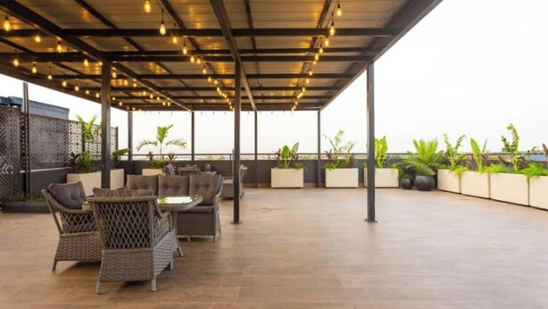 Un patio al aire libre con mobiliario de mimbre, luces colgantes y plantas en macetas.