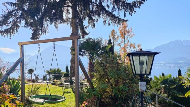 Een tuin met een schommel, een lantaarnpaal en uitzicht op een meer en bergen.