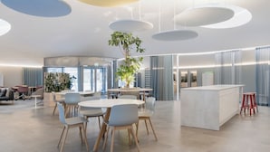 Un moderno vestíbulo de hotel con mesas redondas, asientos cómodos, una planta central y una amplia recepción.