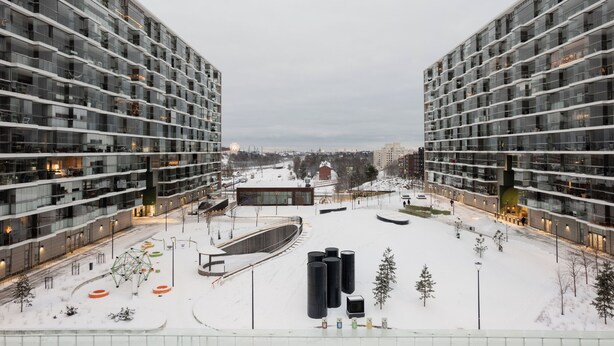 Un complejo moderno de edificios con varios pisos, un espacio central abierto con asientos y suelo cubierto de nieve.