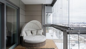 Un balcón moderno con una zona de estar circular con cojines y barandilla de vidrio.