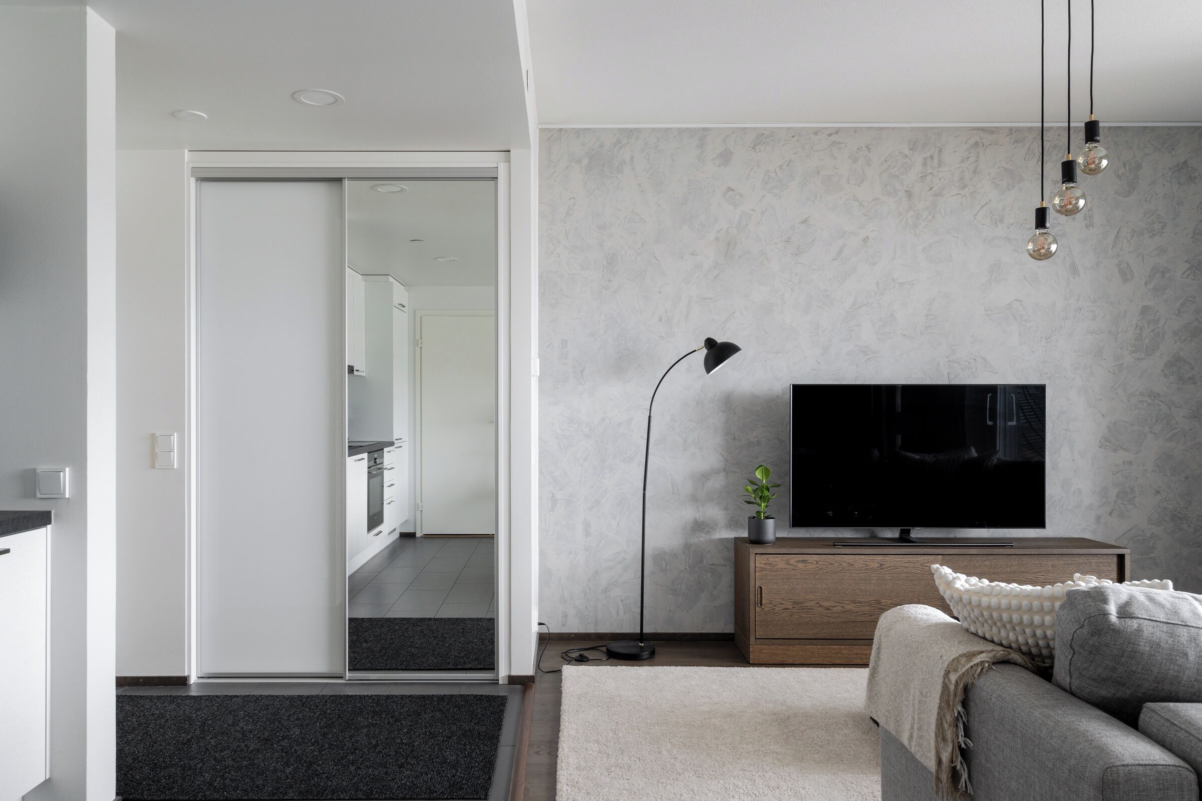 A modern living room with a flat-screen TV, a wooden cabinet, a floor lamp, and a sofa.