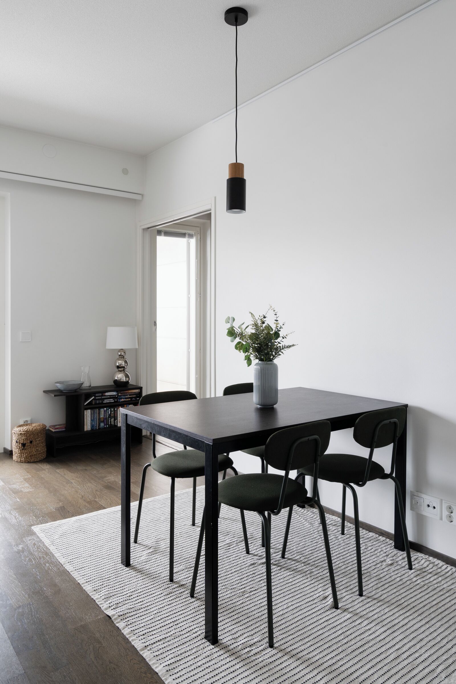 Uma zona de refeições moderna com uma mesa de madeira escura, cadeiras pretas e um lustre.