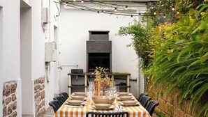 Un'area pranzo all'aperto con tovaglia a quadri, sedie nere e un vaso centrale con fiori.