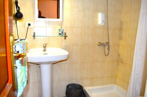 A bathroom with a white sink, a glass shelf with toiletries, a shower, and a trash bin. - Ziggy's Mountain Retreat (Vilaflor)