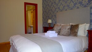 Un letto ben rifatto con lenzuola bianche e una coperta grigia, una lampada da comodino e uno specchio con cornice rossa.