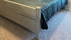 Ein Bett mit Holzrahmen, einer gesteppten grünen Bettdecke und mehreren Kissen in verschiedenen Farben.