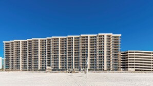 A multi-story hotel with a uniform exterior, numerous balconies, and a sandy foreground.