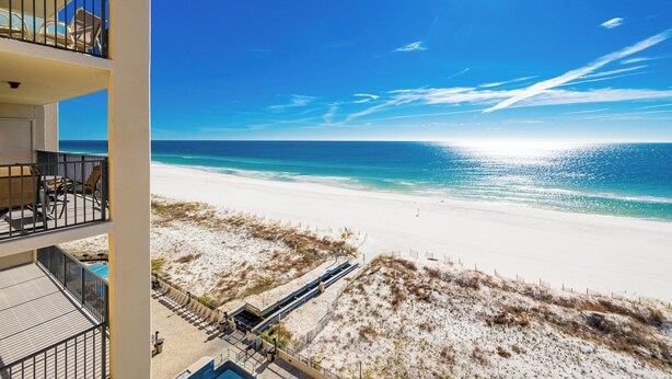 Un hotel frente a la playa con balcones que dan al océano, una playa de arena y cielos despejados.