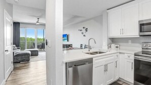 A modern kitchen with stainless steel appliances, white cabinetry, and a large window overlooking a balcony. - Free Golf Cart Rental in 2026! Bayfront Townhouse w/Heated Pool, HotTub, Beach (Ruskin)