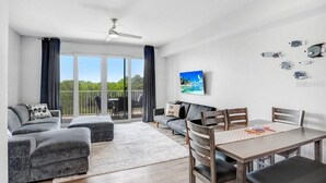 A spacious living area with a balcony, a dining table with chairs, a sofa, and a TV mounted on the wall. - Free Golf Cart Rental in 2026! Bayfront Townhouse w/Heated Pool, HotTub, Beach (Ruskin)