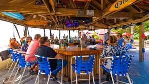 An outdoor bar area with wooden beams, blue chairs, and Corona beer signs. - Free Golf Cart Rental in 2026! Bayfront Townhouse w/Heated Pool, HotTub, Beach (Ruskin)
