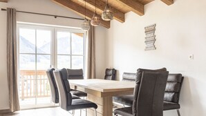 Et spiseområde med et træbord, fire stole, trælofter og udsigt til bjerge gennem store vinduer.