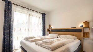 En pænt redt seng med hvide sengetøj og puder, et træhovedgærde og et natbord med en lampe.