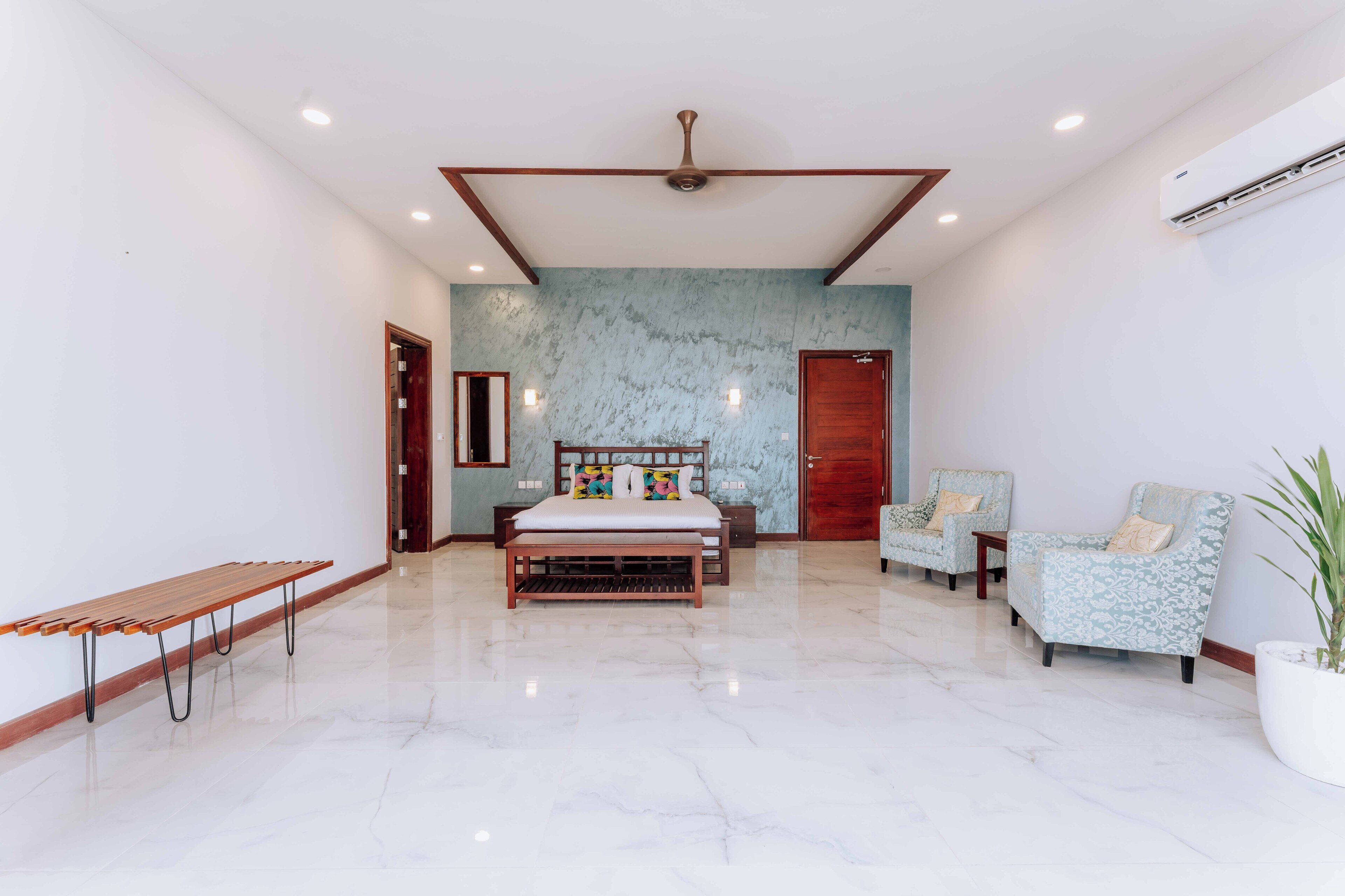 Una habitación amplia con una cama grande, dos sillones, un banco y una planta en maceta.