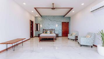 Una habitación amplia con una cama grande, dos sillones, un banco y una planta en maceta.