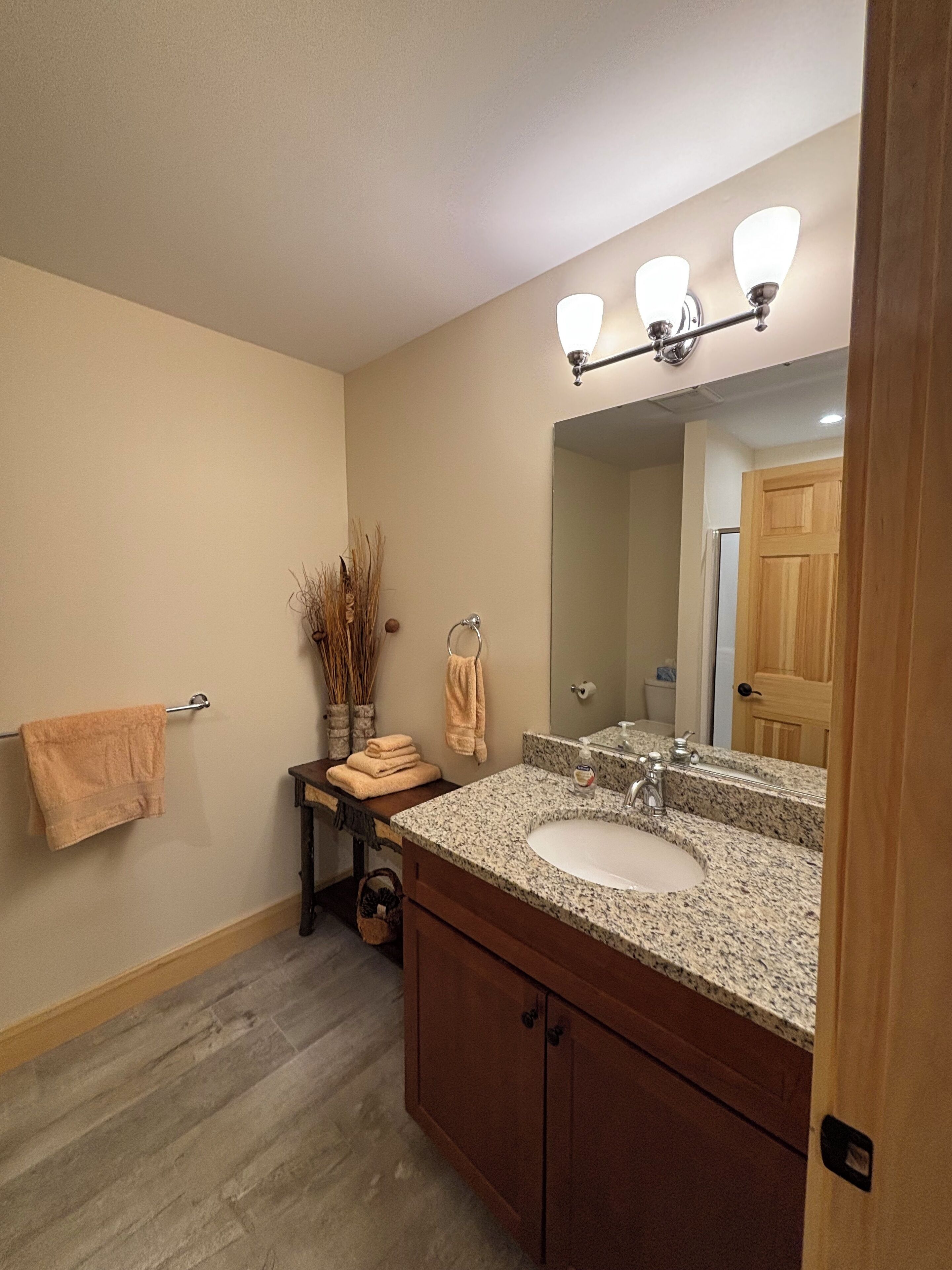 A bathroom with a granite countertop sink, wooden cabinets, a towel rack, and a mirror with lights.