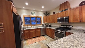 A kitchen with wooden cabinets, granite countertops, a stainless steel refrigerator, a microwave, an oven, and a window with blinds. - Spacious 4-bedroom Ski- in/ Ski-out condo in enchanting Sunday River w/ Hot Tub  (Newry)