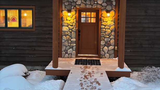 A log cabin with a stone entrance and a wooden porch. - Spacious 4-bedroom Ski- in/ Ski-out condo in enchanting Sunday River w/ Hot Tub  (Newry)