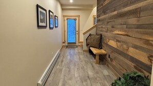 A hallway with a wooden wall panel, a bench, and framed pictures on the wall. - Spacious 4-bedroom Ski- in/ Ski-out condo in enchanting Sunday River w/ Hot Tub  (Newry)