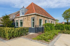Une maison à deux étages, avec un toit recouvert de tuiles rouges, des murs en briques et une entrée fermée par un portail.