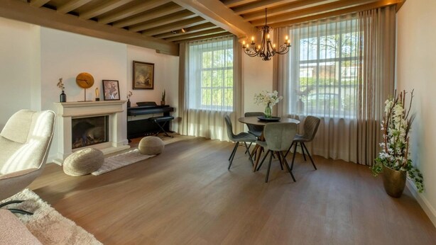 A living room with a fireplace, a dining table with chairs, a piano, and a chandelier. - Farmhouse in Zeeland with Windmill Views (Heinkenszand)