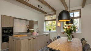 A modern kitchen with a central island, wooden cabinets, and a dining area with a large table and chairs. - Farmhouse in Zeeland with Windmill Views (Heinkenszand)