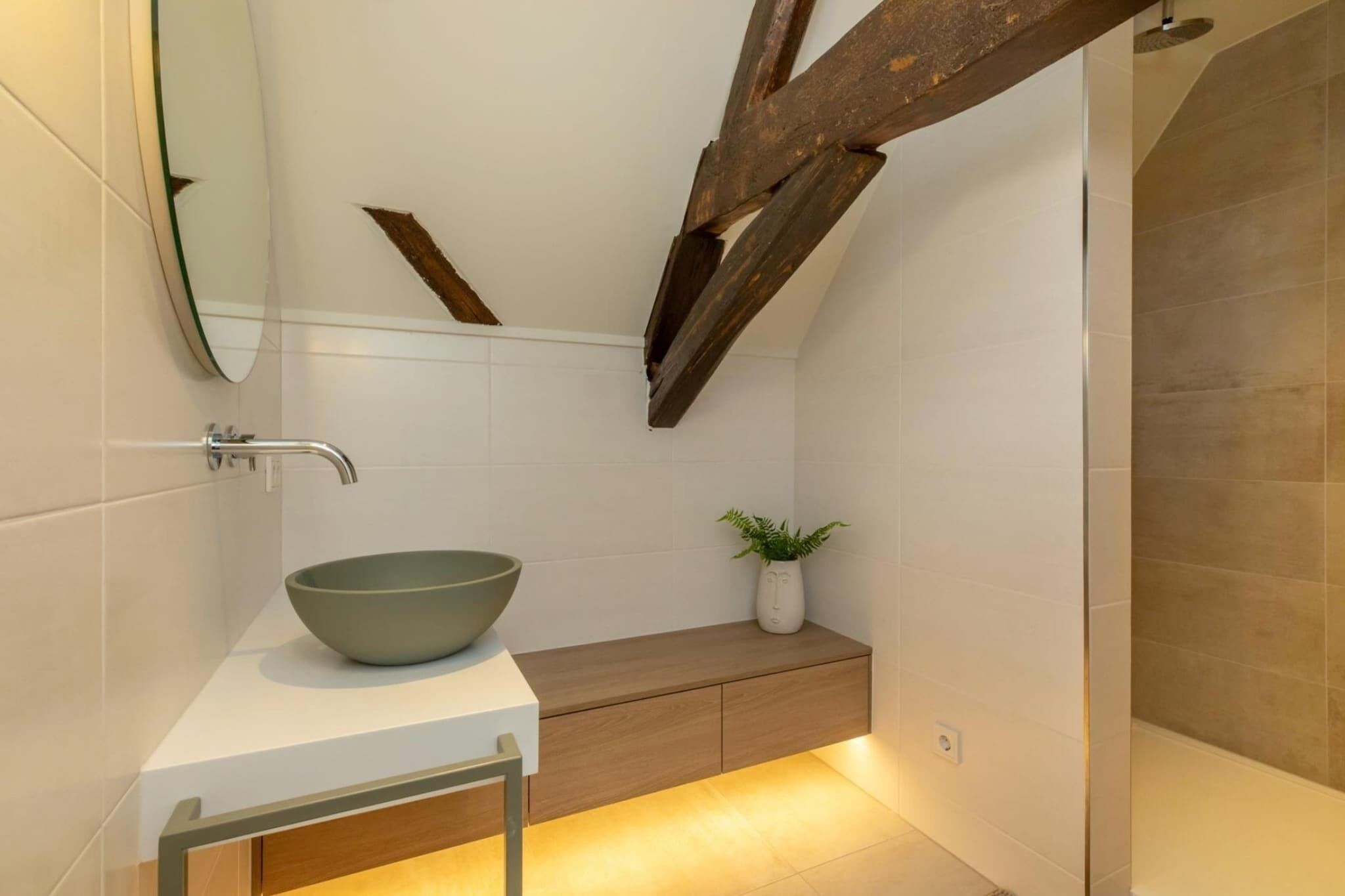 A modern bathroom with a large mirror, a bowl sink, a wooden vanity, and a shower area.
