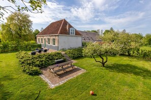 Une maison avec un toit en pente, une terrasse avec une table et des chaises, et une pelouse bien entretenue.