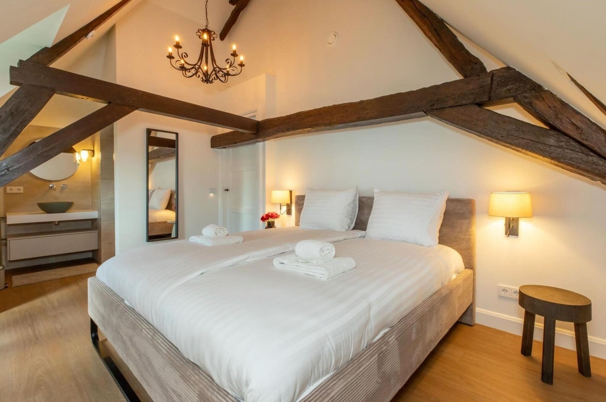 Une chambre à coucher avec un grand lit, des poutres en bois, un lustre et des lampes de chevet.
