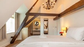 A bedroom with a large bed, wooden beams, a chandelier, a mirror, and a small table with a vase of flowers. - Farmhouse in Zeeland with Windmill Views (Heinkenszand)