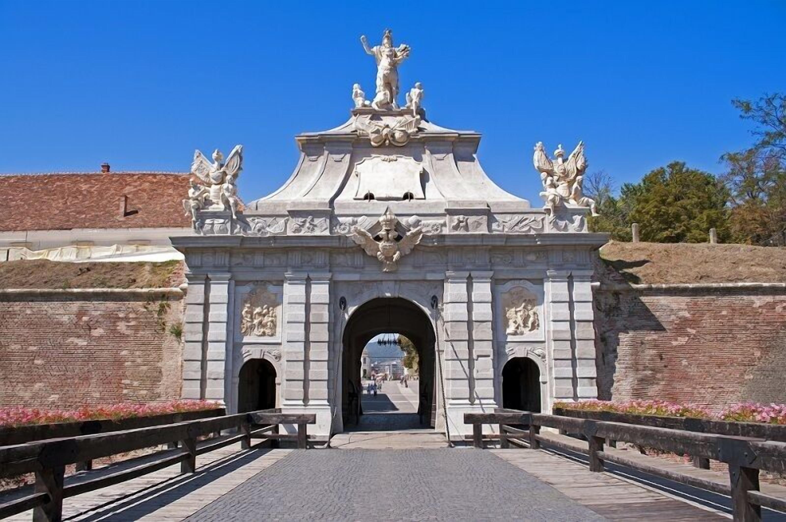 Ein historischer Steinbogen mit aufwendigen Schnitzereien und Statuen, der zu einem Weg führt.