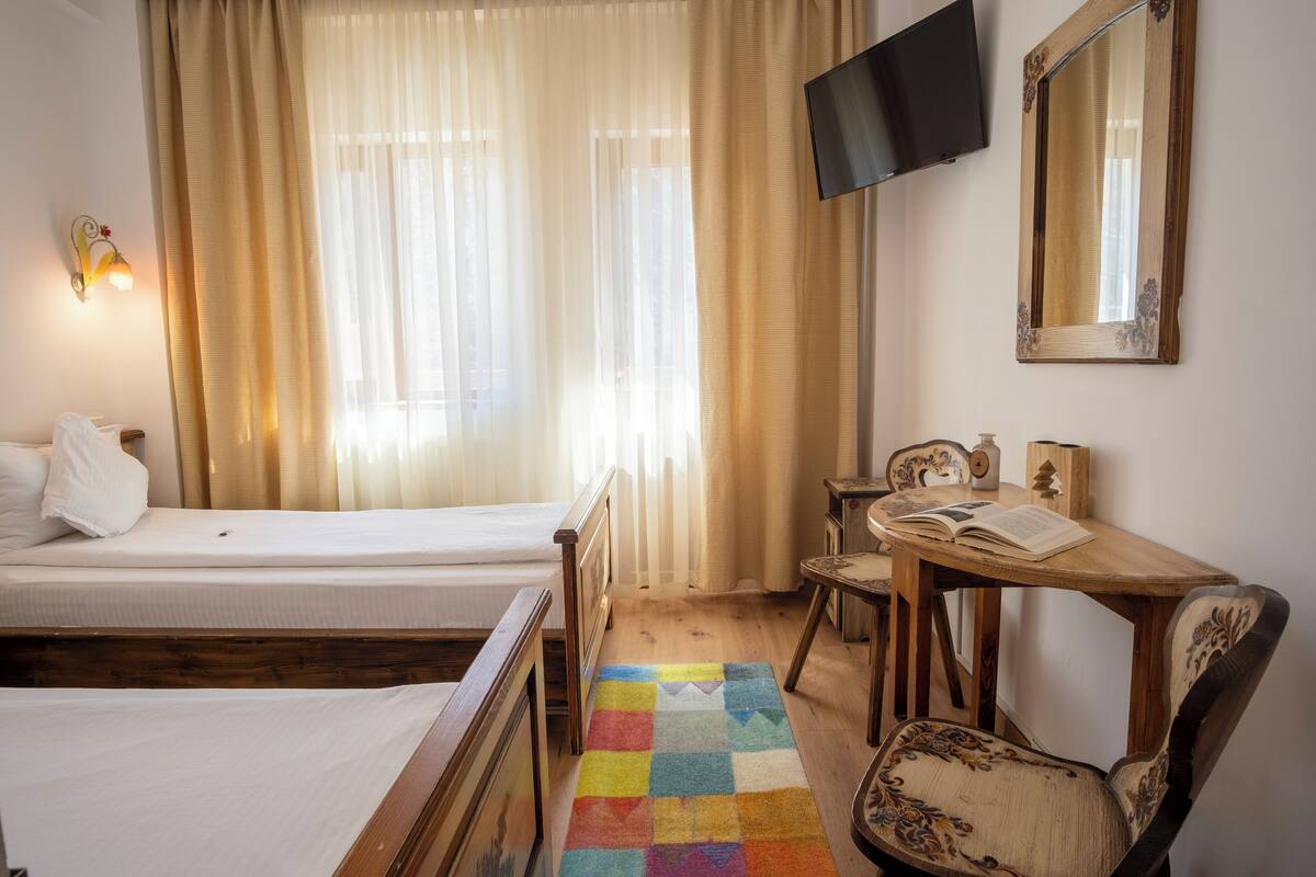 Ein Hotelzimmer mit Bett, Schreibtisch mit Stuhl, Fernseher und einem Fenster mit Vorhängen.