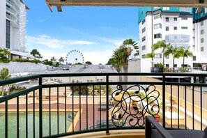 Un balcone con vista su una ruota panoramica, palme e palazzi moderni.