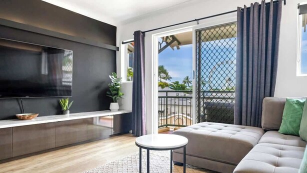 A modern living room with a flat-screen TV, a sofa, a small round table, and a balcony with curtains.