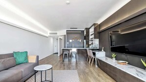 A modern living room with a sofa, a small round table, and a kitchen area with a bar and seating.