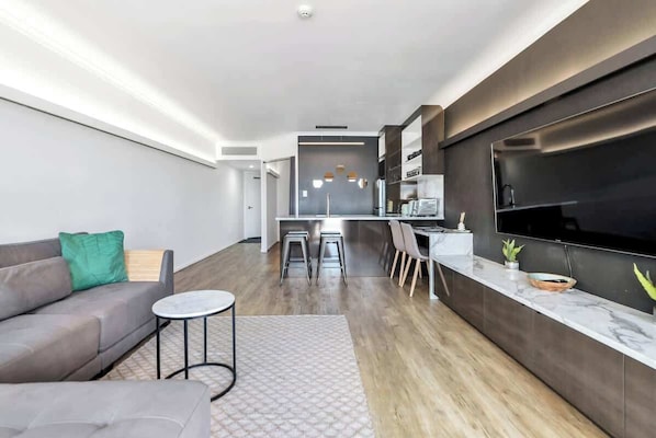 A modern living room with a sofa, a small round table, and a kitchen area with a bar and seating.