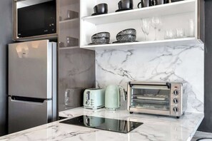 A modern kitchen with a built-in microwave, a stainless steel refrigerator, a toaster, a kettle, and a toaster oven.