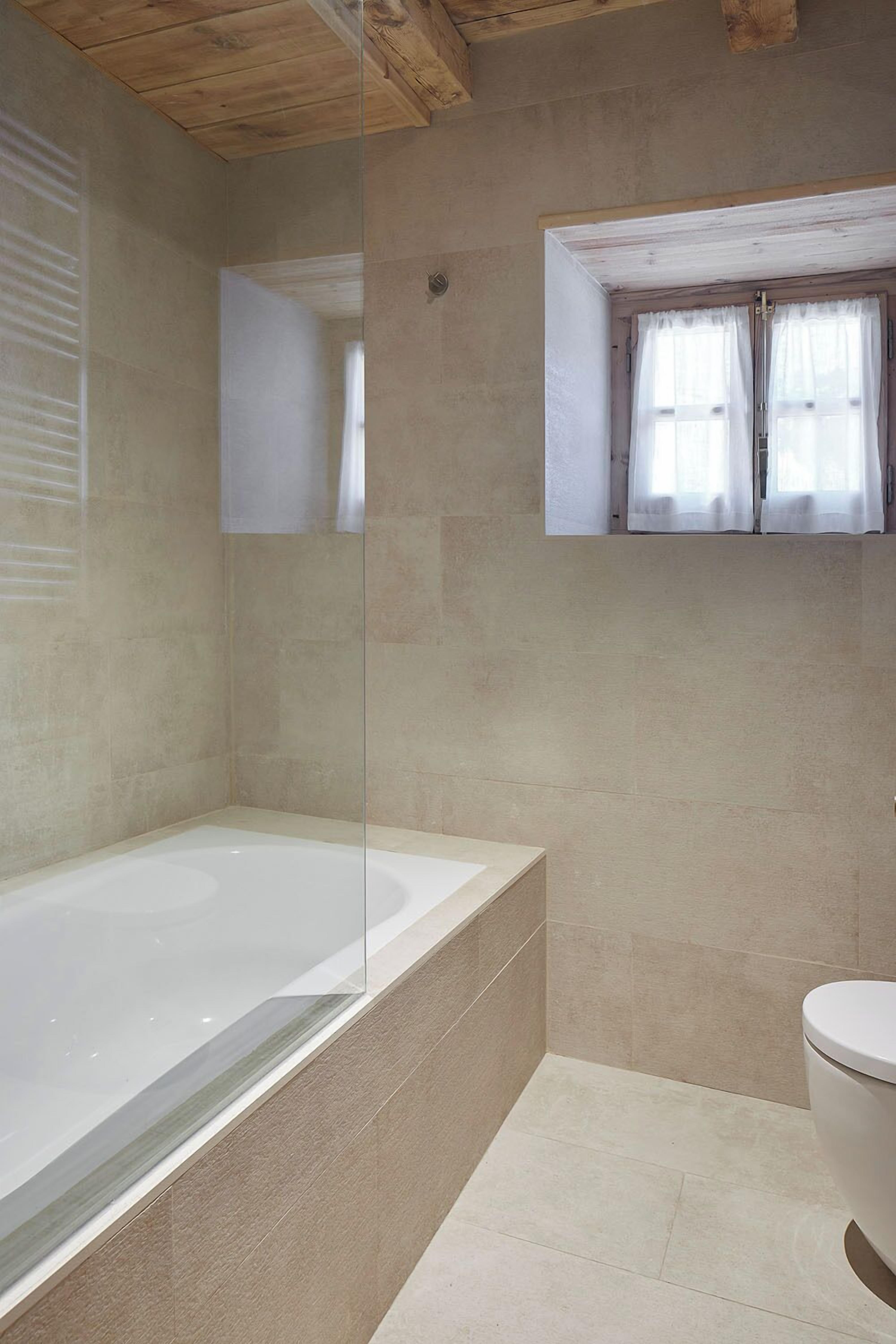 A bathroom with a bathtub, toilet, and a window with curtains.