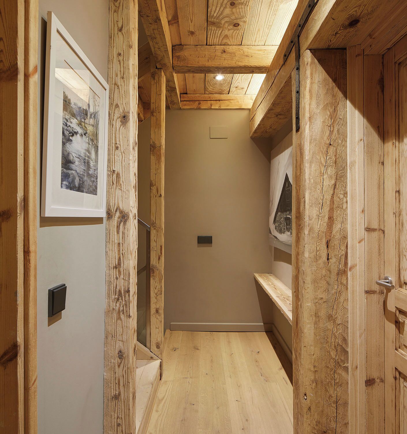 A narrow hallway with wooden walls and ceiling, a framed picture on the left, and a shelf with a picture on the right.