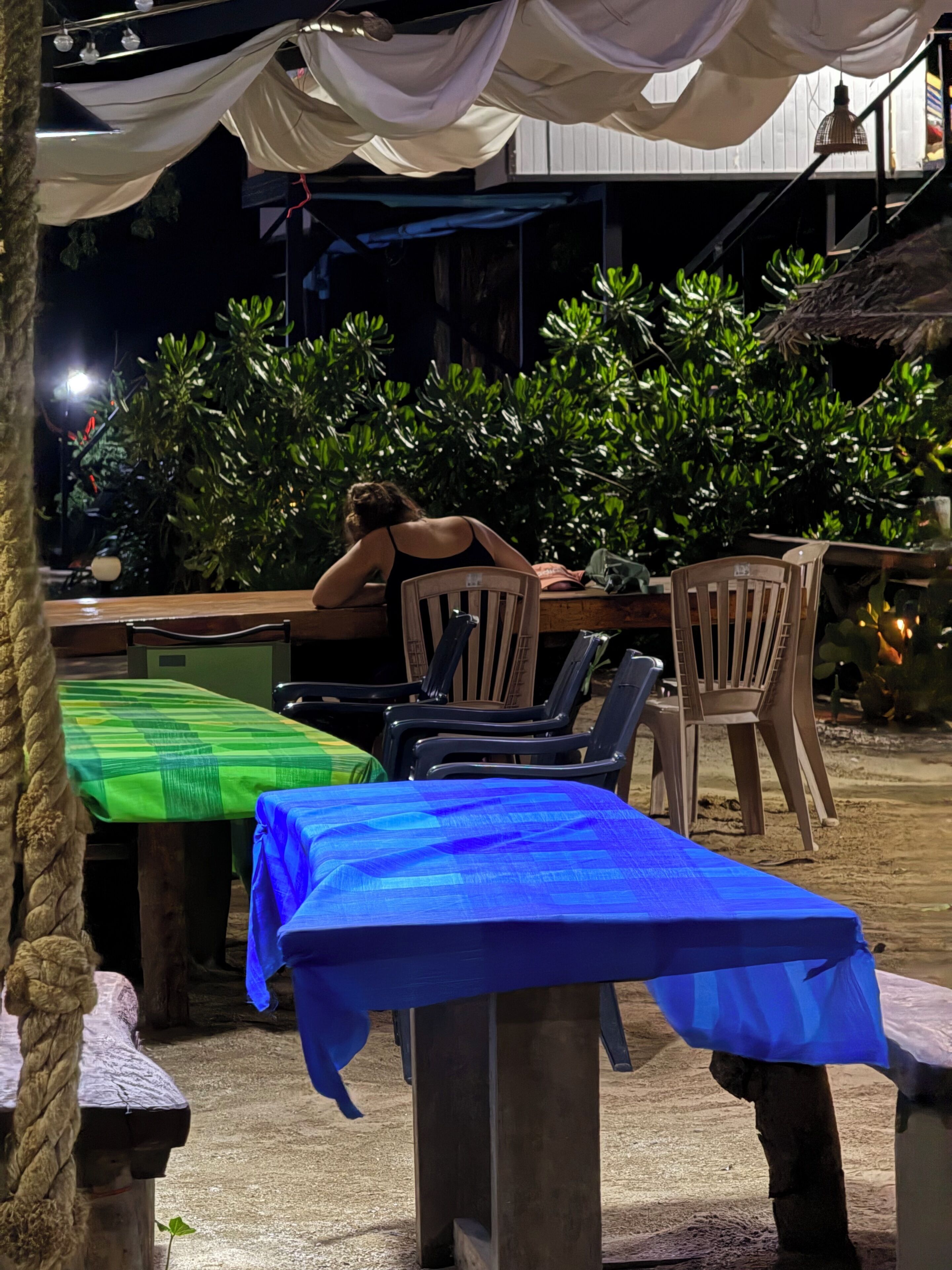 Un espace de restauration en plein air avec des tables recouvertes de nappes vertes et bleues, entourées de chaises et de plantes.