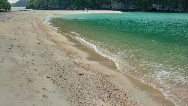 A beach with clear turquoise water, a sandy shore, and a large green hill in the background. - Baan Plai Laem Resort (Ko Phaluai)