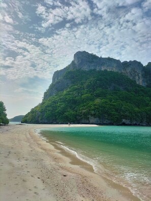 Una playa con aguas turquesas cristalinas, una orilla de arena y una gran colina verde al fondo.