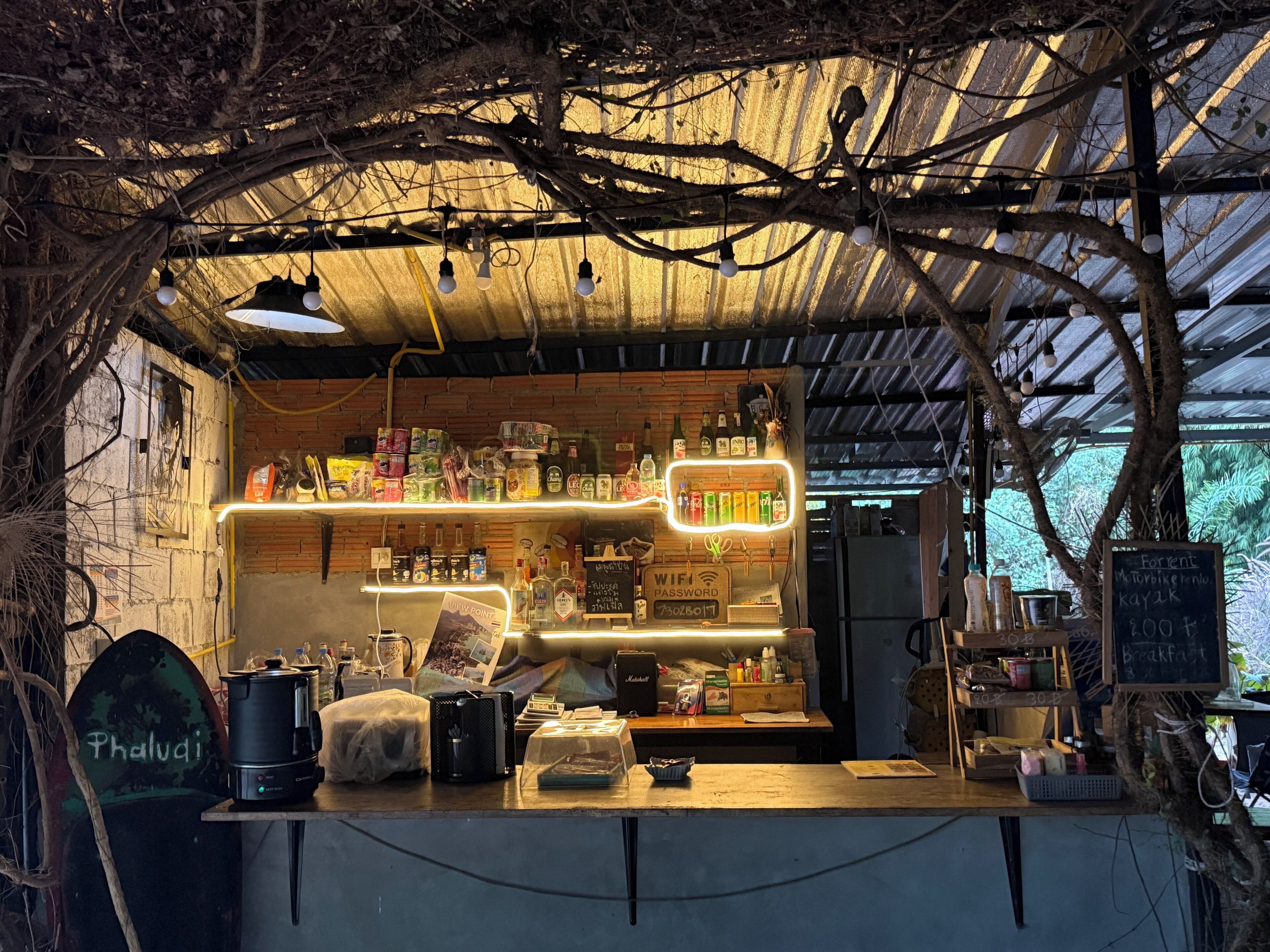 Un café al aire libre rústico con mostrador de madera, diversas bebidas y una pizarra con el menú.