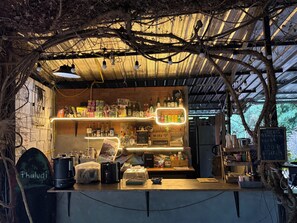 A rustic outdoor café with a wooden counter, various beverages, and a chalkboard menu.