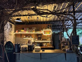 Un café al aire libre rústico con mostrador de madera, diversas bebidas y una pizarra con el menú.