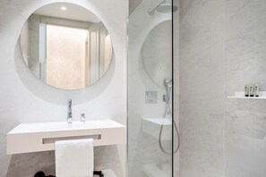 A modern bathroom with a round mirror, a white vanity, a glass-enclosed shower, and a towel rack. - "La Bella Easo" new, ac, design, near La Concha (Donostia-San Sebastian)