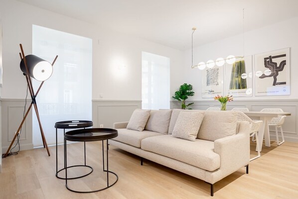 A modern living room with a sofa, a coffee table, and a floor lamp. There is a dining area with chairs and a table. - "La Bella Easo" new, ac, design, near La Concha (Donostia-San Sebastian)